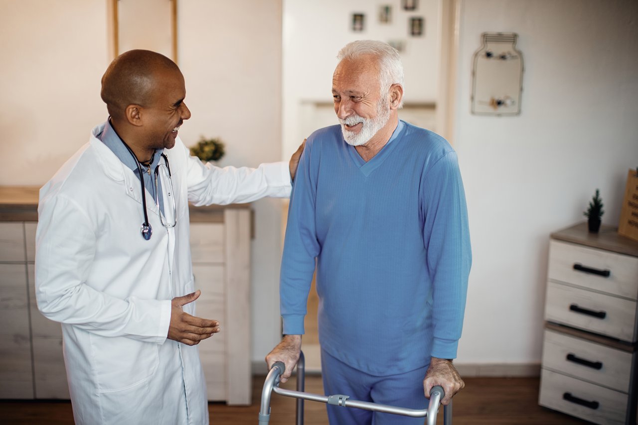 A doctor talking to an older man in blue shirt and white pants.